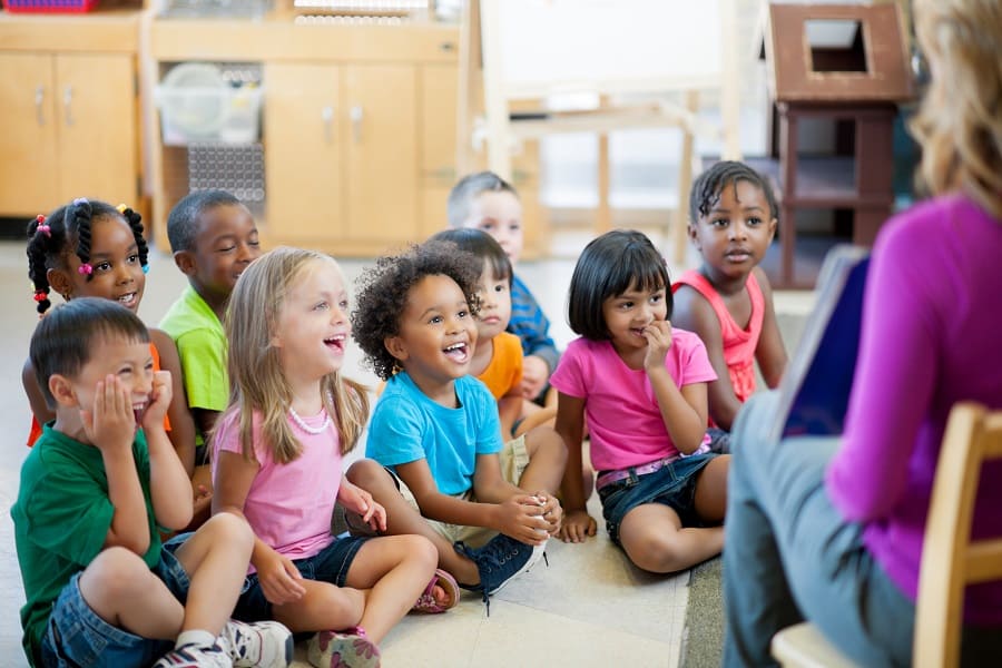 bambini seduti a cerchio che ascoltano entusiasti la maestra