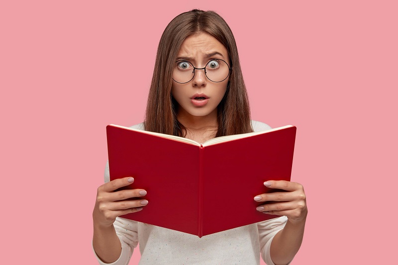 Donna bianca giovane con espressione spaventata che tiene un libro rosso aperto tra le mani